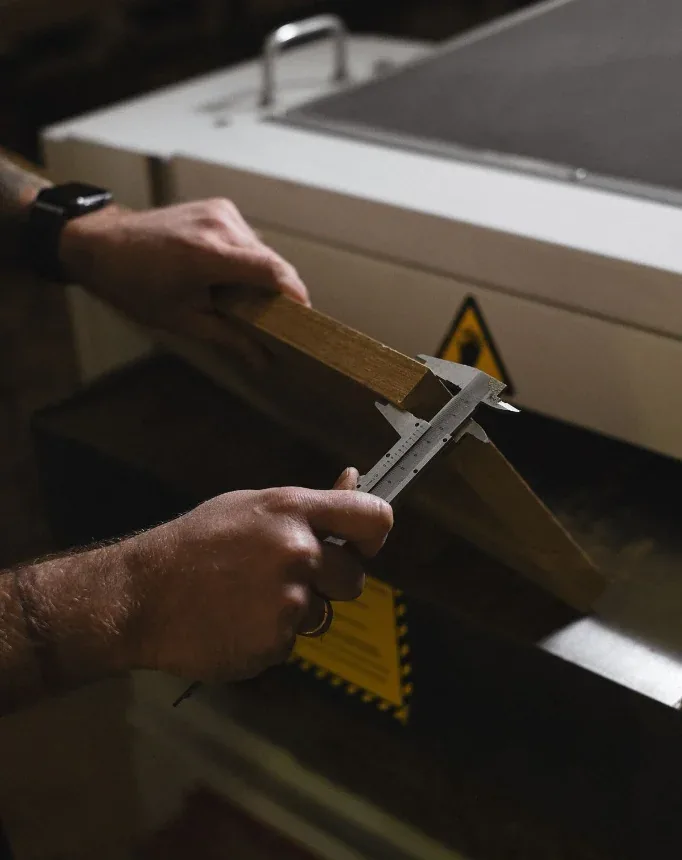 Hands measuring a machined metal workpiece with a precision vernier caliper