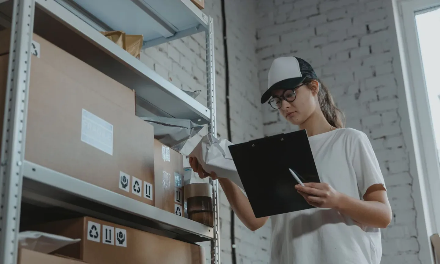 Quality inspector holding a checklist clipboard while examining packaged goods from corrugated shipping cartons