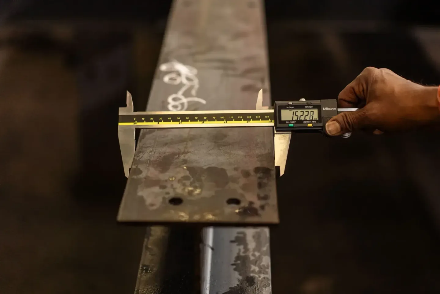 Inspector measuring the thickness of a steel component with a digital caliper